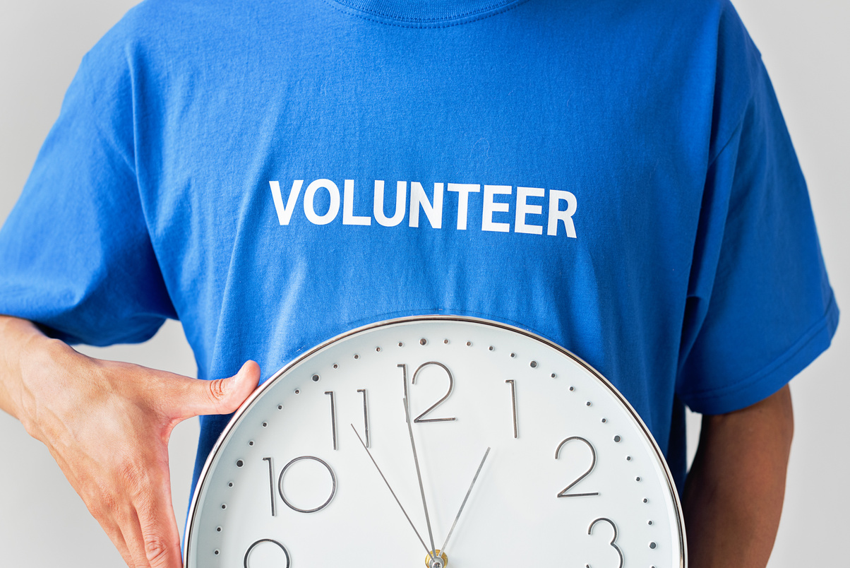 Person In Blue Shirt With Printed Volunteer Text Holding A Wall Clock